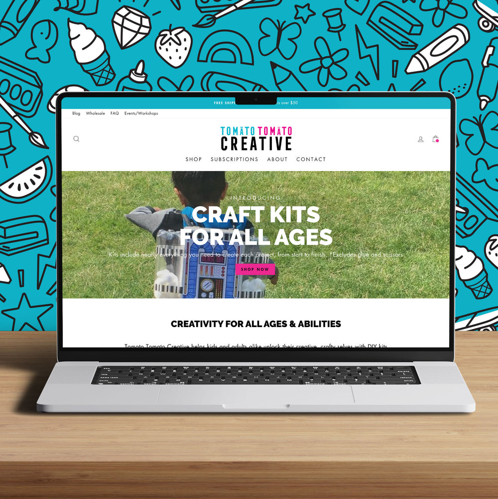 Mockup of Tomato Tomato Creative's Shopify website on a laptop that is sitting on a wooden table. A bright blue hand illustrated pattern design is in the background.